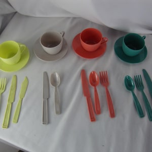May include: A collection of colorful plastic tea cups with saucers and matching cutlery. The set includes yellow, gray, orange, and teal cups, saucers, spoons, forks, and knives, perfect for a vintage tea party.