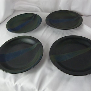 May include: Set of four black ceramic dinner plates with a blue and green glaze. The plates have a wavy design.