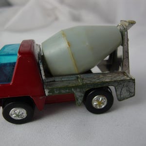 May include: A vintage toy cement mixer truck. The cab is red with a blue windshield, and the mixer is gray. The truck has black wheels with silver hubcaps. The truck is a classic toy.