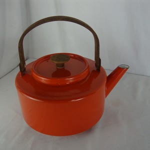 May include: A vibrant orange enamel teapot with a wooden handle and lid knob. The teapot has a rounded body, a spout, and a lid. The handle is arched and made of wood. The teapot is a classic kitchenware item.