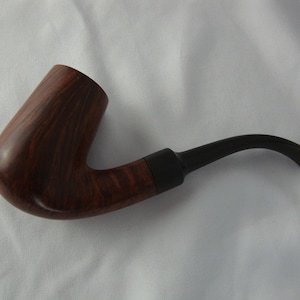 May include: A classic tobacco pipe with a curved stem. The bowl is made of dark brown wood with a visible grain pattern. The stem is black and curves gently downward. A dark band connects the bowl and stem.