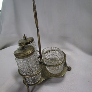 May include: A silver-plated condiment set with three glass containers. The containers have a diamond-shaped pattern and are held together by a metal stand with a handle.