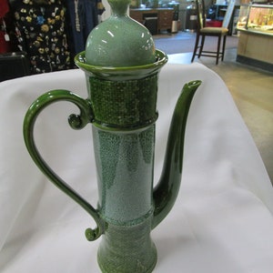 May include: A green ceramic teapot with a lid and a textured surface. The teapot has a handle and a spout.