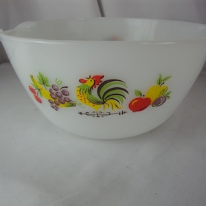 May include: White mixing bowl with a colorful rooster and fruit design. The bowl has two handles and a wide opening. The rooster is yellow, red, green, and black. The fruit includes grapes, bananas, apples, and plums.