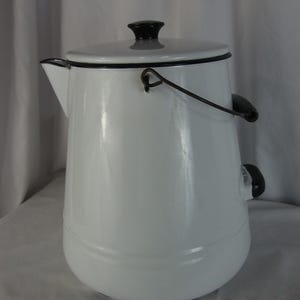 May include: A white enamel coffee pot with a black handle, lid, and rim. The pot has a spout for pouring and a curved handle. The lid has a black knob. The pot is a classic design, suitable for brewing coffee.
