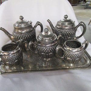 May include: A silver tea set with a teapot, creamer, sugar bowl, and tray. The set has a decorative, embossed design.
