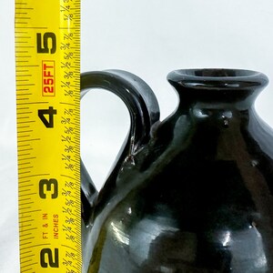 Puede incluir: Una jarra de cer&aacute;mica verde oscuro con asa. La jarra tiene un cuerpo redondeado y un peque&ntilde;o pico.
