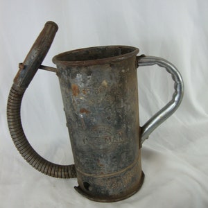 May include: A vintage metal watering can with a long, flexible hose. The can is rusty and has a silver handle. The can has the words "Fireman" and "Made in USA" printed on it.