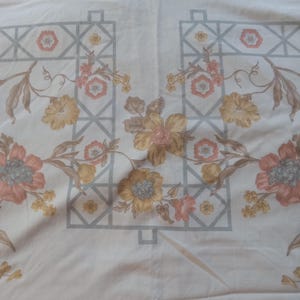 May include: White fabric with a floral pattern. The pattern features pink, yellow, and brown flowers with green leaves. A gray geometric pattern is in the background.