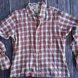 May include: A long-sleeved button-down shirt in a red, white, and blue plaid pattern. The shirt has a classic collar and a single chest pocket. The fabric appears to be lightweight, suitable for warmer weather.