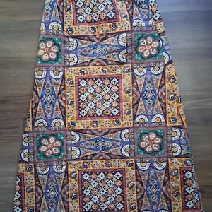 May include: A long, patterned skirt with a vibrant, geometric design. The skirt features a patchwork of squares and shapes in shades of blue, yellow, orange, and green. The fabric appears to be lightweight, suitable for warm weather.
