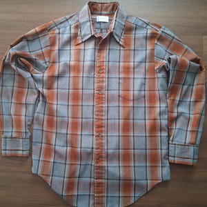 May include: A long-sleeved button-down shirt with a plaid pattern in shades of orange, gray, and brown. The shirt has a pointed collar, a chest pocket, and buttoned cuffs. The fabric appears to be a soft, woven material.