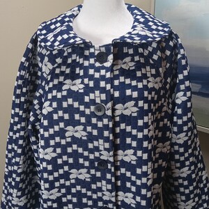May include: A navy blue and white patterned jacket with a floral design. The jacket has a large collar and three dark blue buttons. The fabric has a checkered pattern with white floral accents.