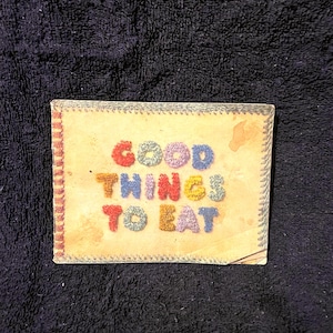 May include: A vintage book cover with the title "GOOD THINGS TO EAT" in colourful yarn letters on a tan background.