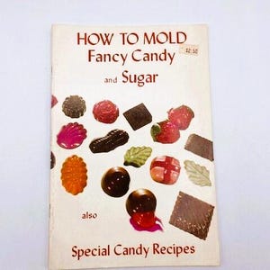 以下が含まれることがあります： 「How to Mold Fancy Candy and Sugar」というタイトルのヴィンテージの料理本で、価格は2.50ドルです。表紙には、ハート、葉、星など、さまざまな形をしたカラフルなモールドキャンディーが並んでいます。