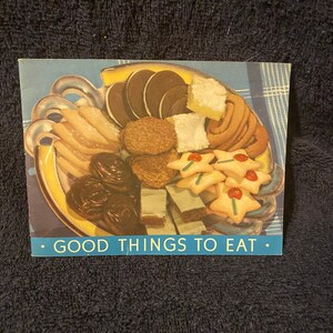 May include: A blue and yellow plate filled with a variety of cookies and pastries. The plate is surrounded by a blue and white checked tablecloth. The text "GOOD THINGS TO EAT." is printed below the plate.