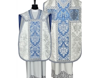 May include: White and blue liturgical vestments with a floral pattern. The chasuble features a cross with the Marian monogram "M" in the center. The stole has a matching design.
