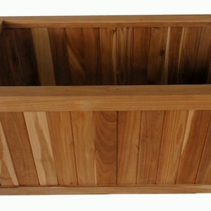 May include: A rectangular wooden planter box with a natural wood finish. The planter has a slatted design and a decorative top trim. The interior is empty, ready for plants. The box is made of light brown wood.