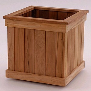 May include: A square wooden planter box with a natural wood finish. The planter has a rectangular opening at the top and is constructed with vertical wooden planks. The design includes a top and bottom trim, suitable for gardens or patios.