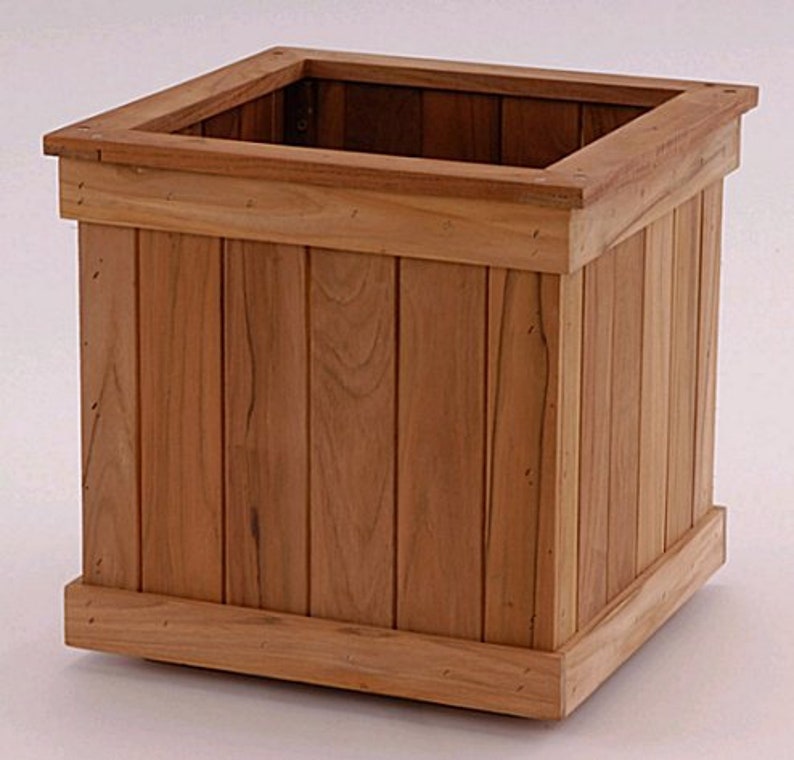 May include: A square wooden planter box with a natural wood finish. The planter has a rectangular opening at the top and is constructed with vertical wooden planks. The design includes a top and bottom trim, suitable for gardens or patios.