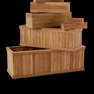 May include: A selection of wooden rectangular planters in various sizes. The planters are made of light brown wood and have a slatted design on the sides. The arrangement includes several stacked boxes, showcasing the different sizes available.