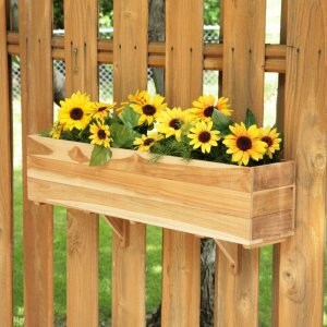 May include: A rectangular wooden planter box filled with vibrant yellow sunflowers. The planter is mounted on a wooden fence with visible support brackets. The sunflowers have dark centers and green leaves.
