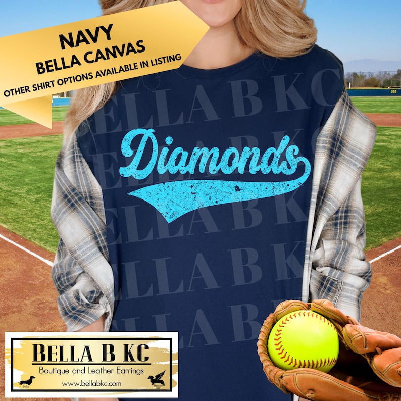 May include: A navy blue t-shirt featuring the word Diamonds in a light blue, distressed, script-style font with a swoosh underline. The shirt is layered under a plaid button-down shirt. A yellow softball is held in a brown leather baseball glove.