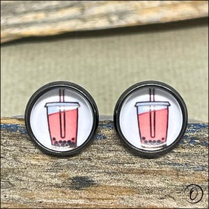 May include: A pair of black stud earrings featuring a white background and a cartoon image of a pink bubble tea with a straw.