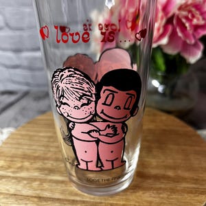 May include: Clear glass with a cartoon illustration of two figures embracing, with the words "love is..." and "TOGETHERNESS" printed on the glass. Red hearts and text accents the design.