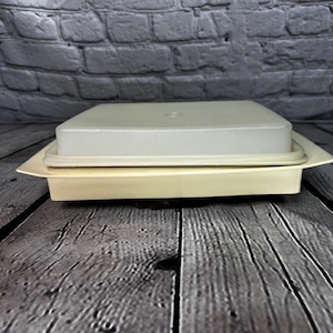 May include: A white plastic serving dish with a lid. The dish is on a wooden surface.