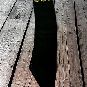 May include: A black fabric sash with three yellow and brown scout badges attached. The badges feature a railway crossing, a campfire, and a compass.