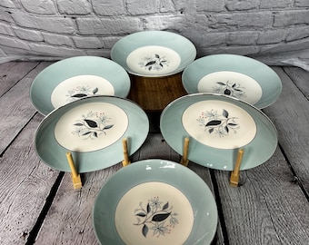 May include: Set of six blue and white ceramic salad plates with a floral design. The plates have a light blue rim and a white center with a stylized floral pattern in black and red.