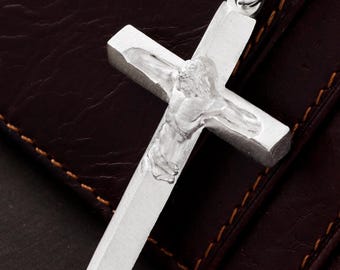 May include: A silver-toned metal crucifix pendant featuring a raised, molded figure of Jesus Christ centered on the cross. The pendant is attached to a matching silver-toned link chain, showcasing a polished finish and a simple, clean design.