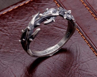 May include: A silver ring featuring a textured, thorn-like design around the band. The interior of the band is engraved with the word Genesis and the hallmark 925, indicating sterling silver composition. The metal has a dark, oxidized finish.