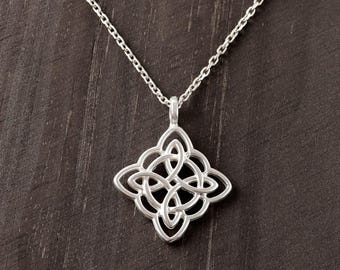 May include: A silver-toned necklace featuring a square-shaped pendant with an intricate, symmetrical openwork knot design. The pendant is suspended from a delicate, thin silver-toned chain that connects to the top of the decorative metal piece.
