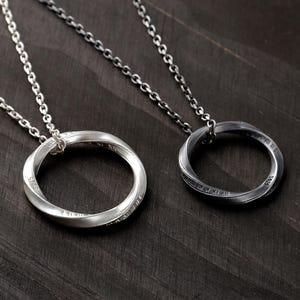 May include: Two circular pendant necklaces on silver-toned chains. One pendant is polished silver, and the other is oxidized dark gray. Both rings feature a twisted design with the engraving S925 visible on the surface of the metal bands.