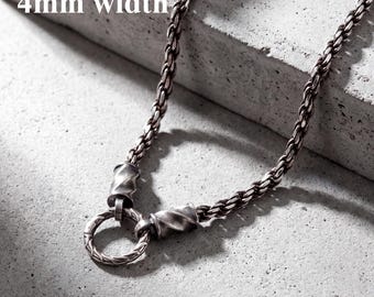 May include: A silver-toned chain necklace featuring a braided link design with a 4mm width. The necklace includes two twisted cylindrical connectors that attach to a circular ring pendant with a matching braided texture and oxidized finish.