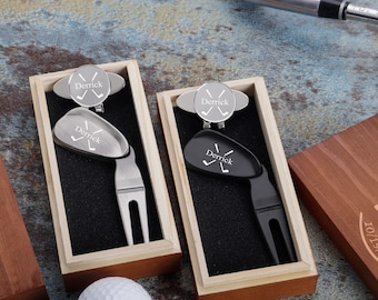 May include: Two wooden boxes with black velvet interiors, each containing a personalized golf ball marker and divot tool. The tools are engraved with the name "Derrick" and crossed golf clubs.