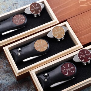 May include: Four wooden boxes with black golf tool sets inside. Each box has a personalized golf ball marker with a name and crossed golf clubs. The names are Roberto, Derrick, Thomas, and Thomas.