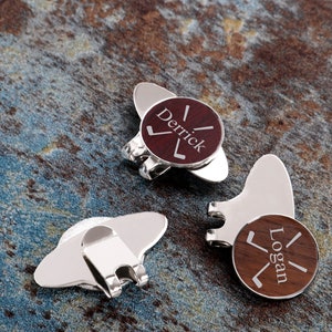 May include: Two silver golf ball markers with wooden inserts. The inserts are engraved with the names "Derrick" and "Logan" and a golf club graphic.
