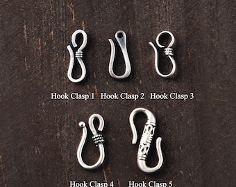 May include: Five silver-toned metal hook clasps for jewelry making, labeled Hook Clasp 1 through Hook Clasp 5. The clasps feature various curved designs, including smooth surfaces and textured, coiled, or patterned details on the metal hooks.