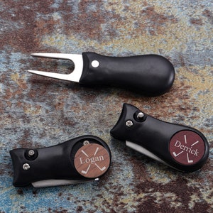 May include: Three black golf divot tools with a wooden insert. The inserts are engraved with the names "Logan" and "Derrick" and a golf club graphic.