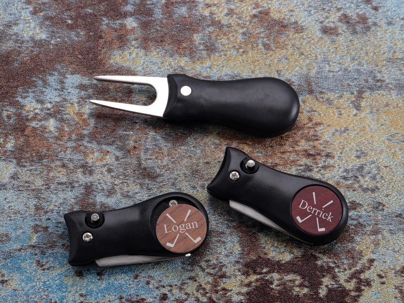 May include: Three black golf divot tools with a wooden insert. The inserts are engraved with the names "Logan" and "Derrick" and a golf club graphic.