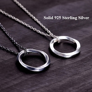 Puede incluir: Dos collares con colgantes circulares trenzados en cadenas de eslabones finos. Un colgante es de plata brillante y el otro de plata oxidada oscura. El texto Solid 925 Sterling Silver es visible en la esquina superior derecha.