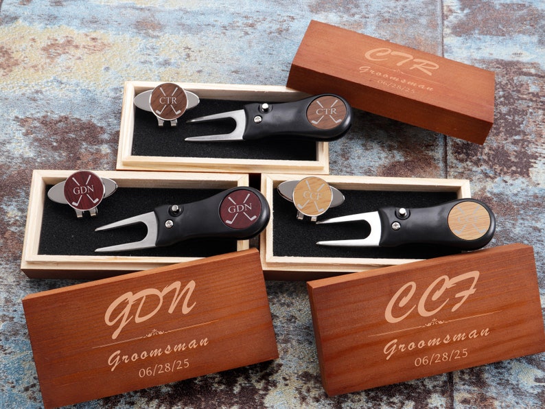 May include: Four wooden boxes with engraved text, each containing a golf ball marker and a golf divot tool. The boxes are labeled with the initials "CTR", "GDN", and "CCF" and the text "Groomsman" and a date.