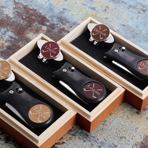 May include: Four wooden boxes each containing a golf ball marker and a golf tool with a personalized name on each. The names are Derrick, Logan, and Lucca.