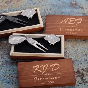 May include: Two wooden boxes with engraved text, each containing a golf ball marker and a divot tool. The boxes are personalized with the names "Austin Evans Frye" and "Kevin John Dolan" and the date "11/18/25".
