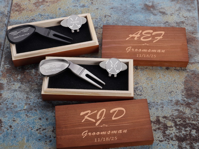May include: Two wooden boxes with engraved text, each containing a golf ball marker and a divot tool. The boxes are personalized with the names "Austin Evans Frye" and "Kevin John Dolan" and the date "11/18/25".