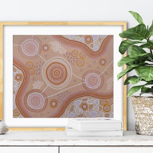Pode incluir: Impress&atilde;o de arte abstrata em uma moldura dourada. A obra apresenta um fundo bege com padr&otilde;es circulares e lineares marrons, roxos e brancos. A impress&atilde;o &eacute; exibida em uma superf&iacute;cie branca com uma planta em uma cesta tecida.