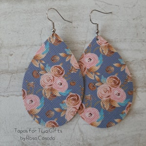 May include: A pair of teardrop-shaped earrings with a floral pattern. The earrings feature a light blue background with pink and brown flowers and silver-colored ear wires. The text "Tapas for Two Gifts by Rosa Casado" is at the bottom.